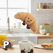 Peluche croissant Amuseables de Jellycat au dessus de la tasse café Jellycat
