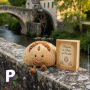 Peluche Pain au Levain Amuseables de Jellycat sur un mur avec moulin à eau